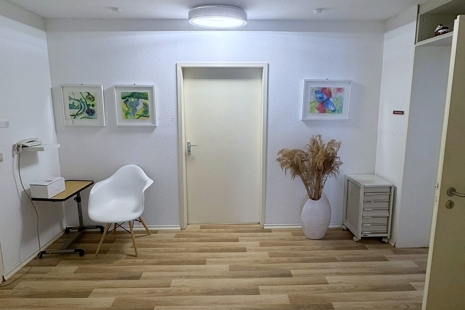 Heller Flur der Praxis mit Bildern an der Wand und Sitzgelegenheit